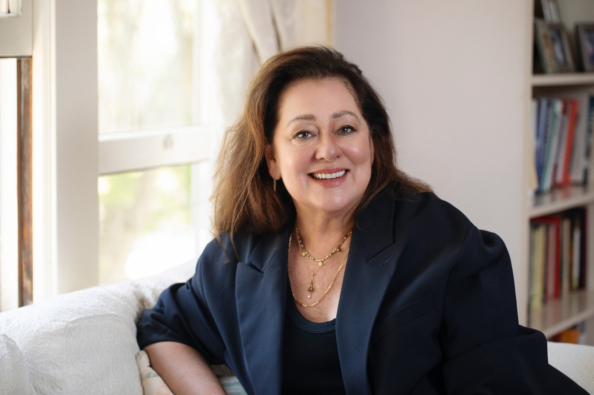 Amanda Twiss in a navy blazer, seated on a white couch